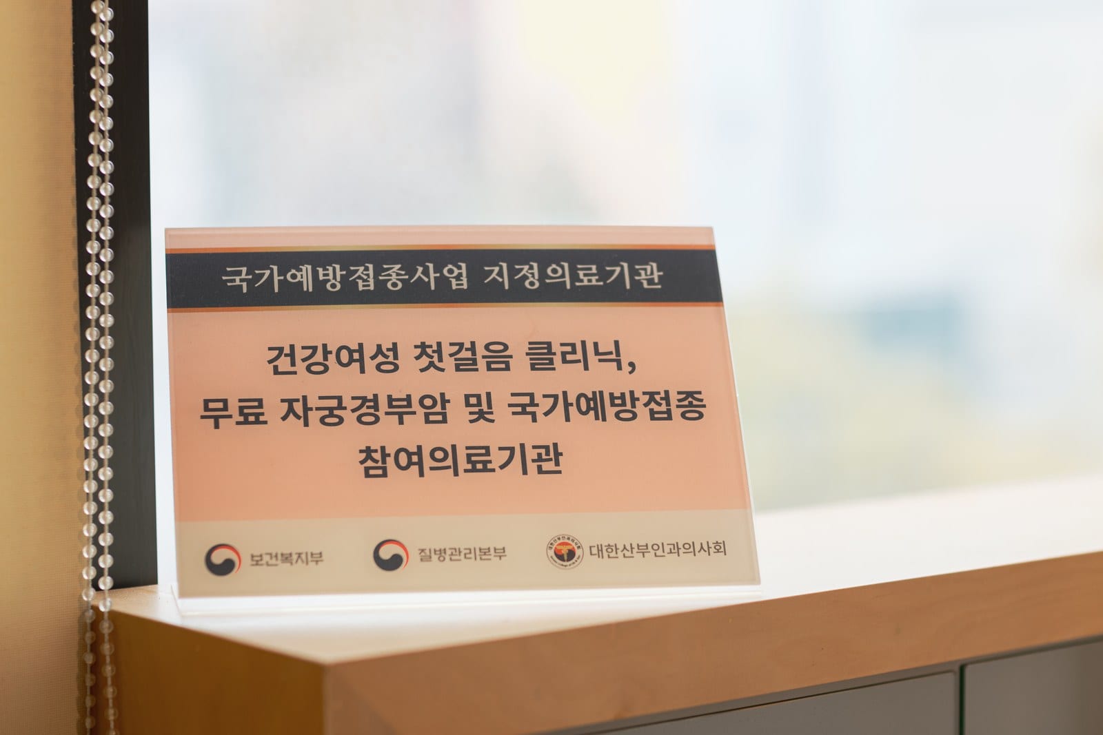 윈산부인과 창가에 놓인 무료 자궁경부암 검진 및 국가예방접종 참여의료기관 안내 명패